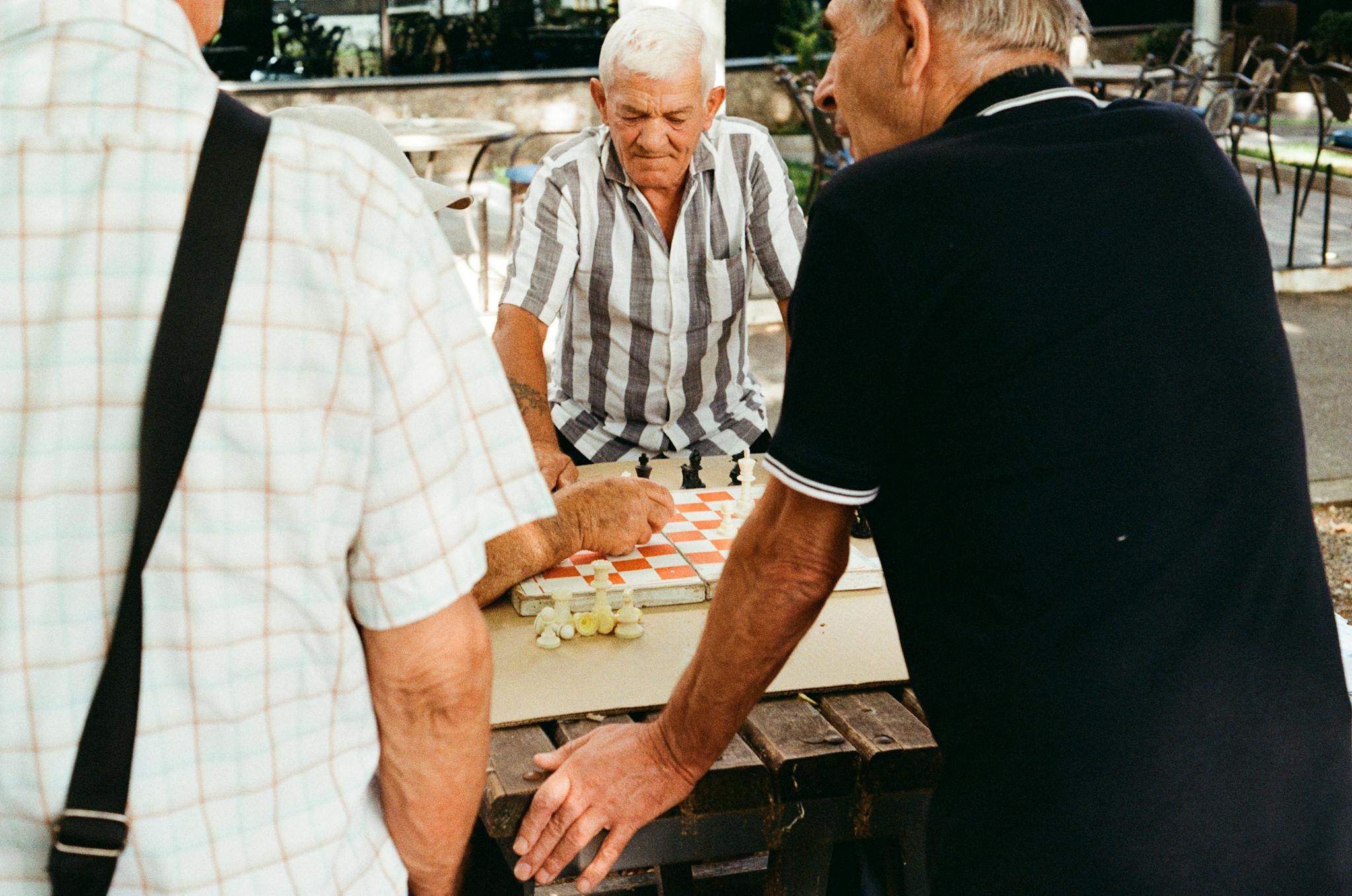 Three senior men playing a chess game outdoors, enjoying a sunny day.